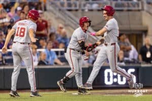 Arkansas Razorbacks Reese Robinett (18) and Brent Iredale, right, celebrates their runs with Charles Davalan against the LSU Tigers in the ninth inning during the College World Series on Wednesday, June 18, 2025 in Omaha, Nebraska. Photo by John S. Peterson.